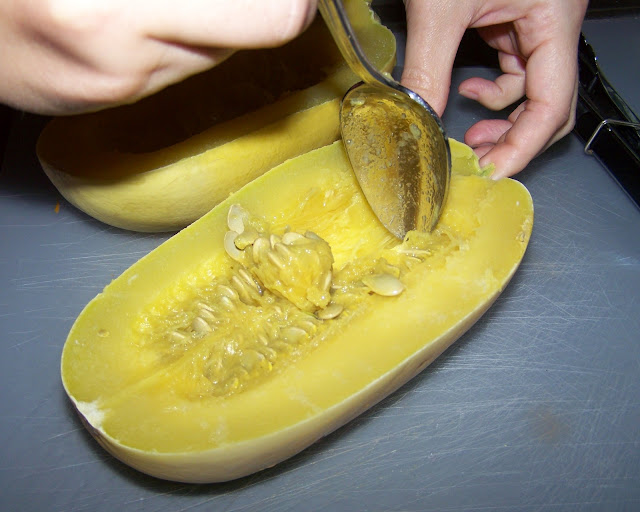Using a spoon to scoop seeds out of a half of a spaghetti squash